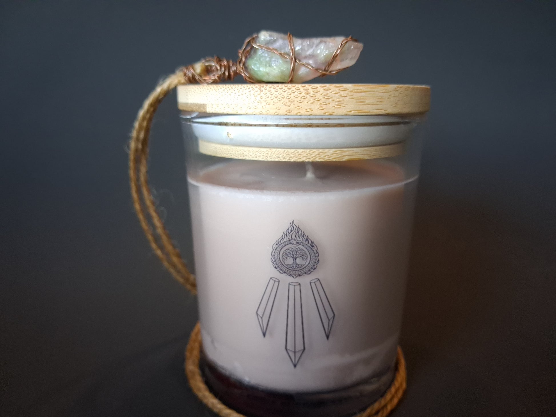 The Knowing candle with bamboo lid topped with wire-wrapped amethyst crystal pendant on jute cord, cream wax with Awen Aboros logo