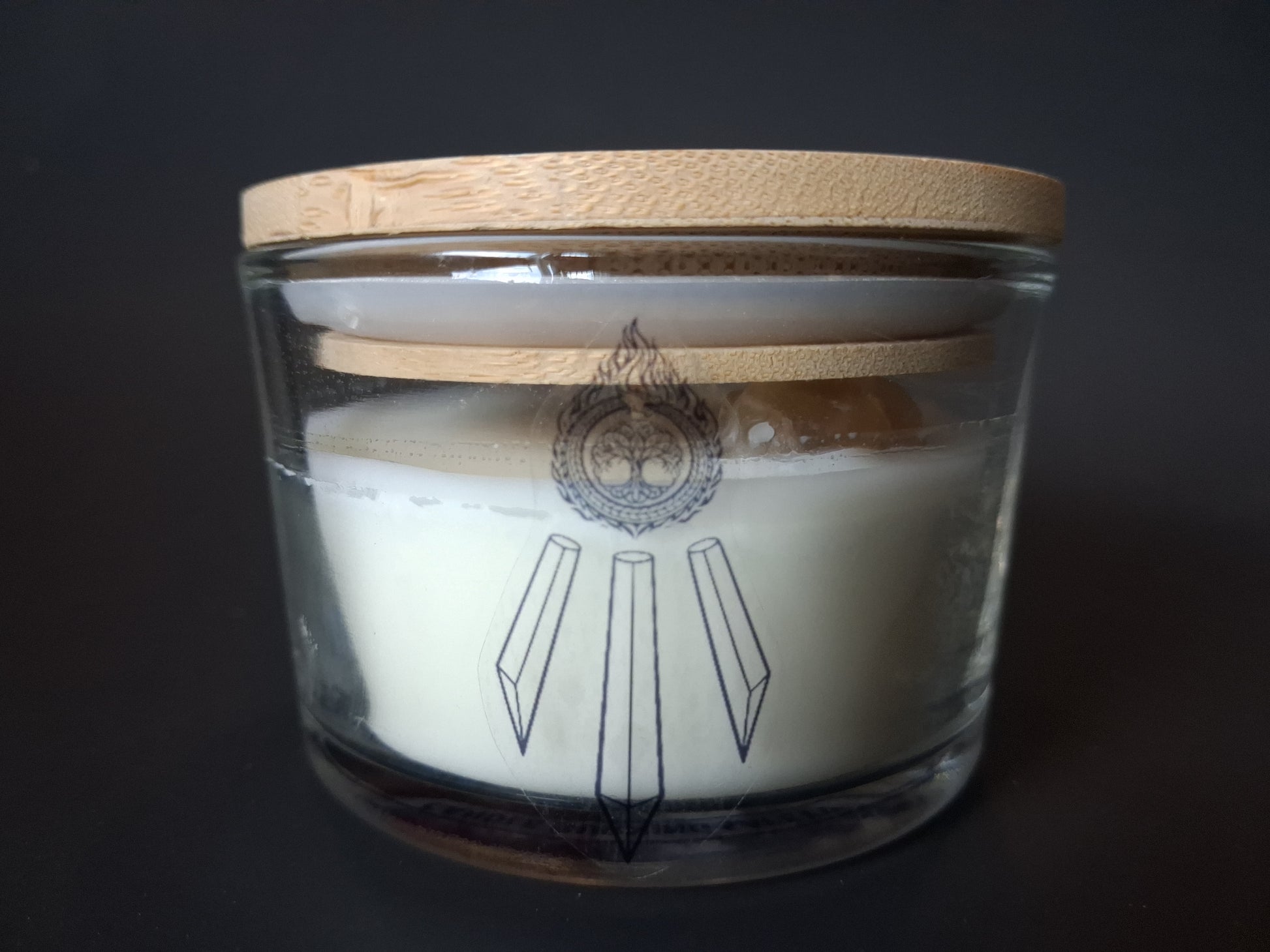 Citrine Intentions candle with plain bamboo lid on wide-mouth clear glass jar, cream wax with Awen Aboros crystal logo, dark background
