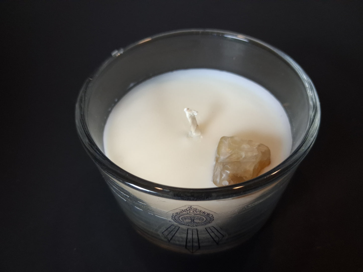 Citrine Intentions candle top-down view showing raw citrine gemstone and wick set in cream wax, Awen Aboros logo etched on clear glass, dark background