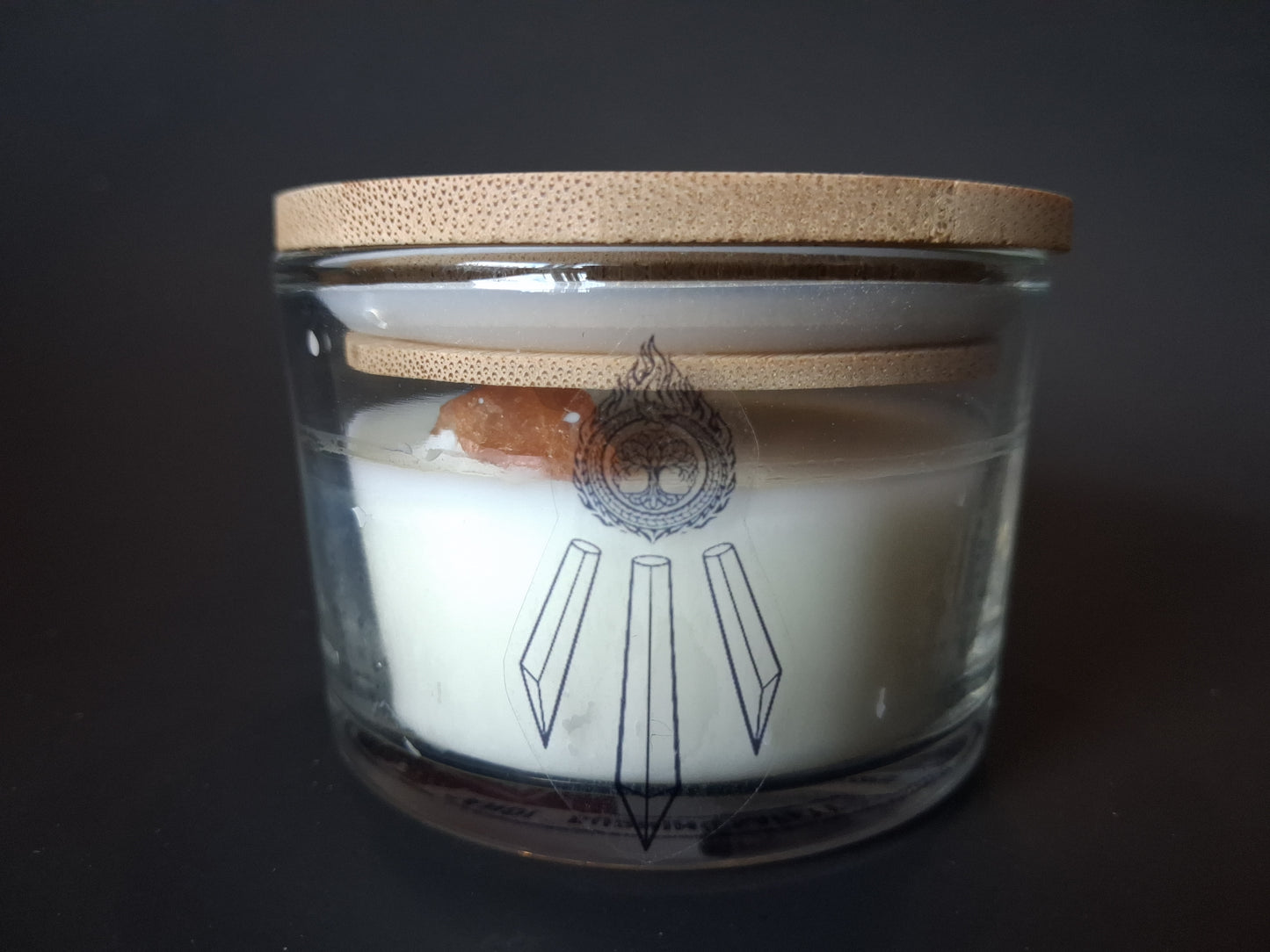 Champagne Aura Intentions candle with bamboo lid, raw Champagne Aura Quartz gemstone visible through clear glass, Awen Aboros crystal and tree logo etched on jar, dark background