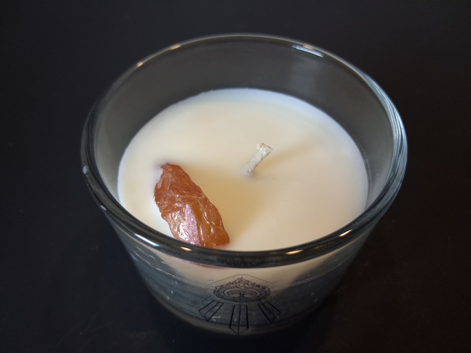 Champagne Aura Intentions candle open from above showing raw champagne aura quartz gemstone and wick set in cream wax, Awen Aboros logo etched on clear glass