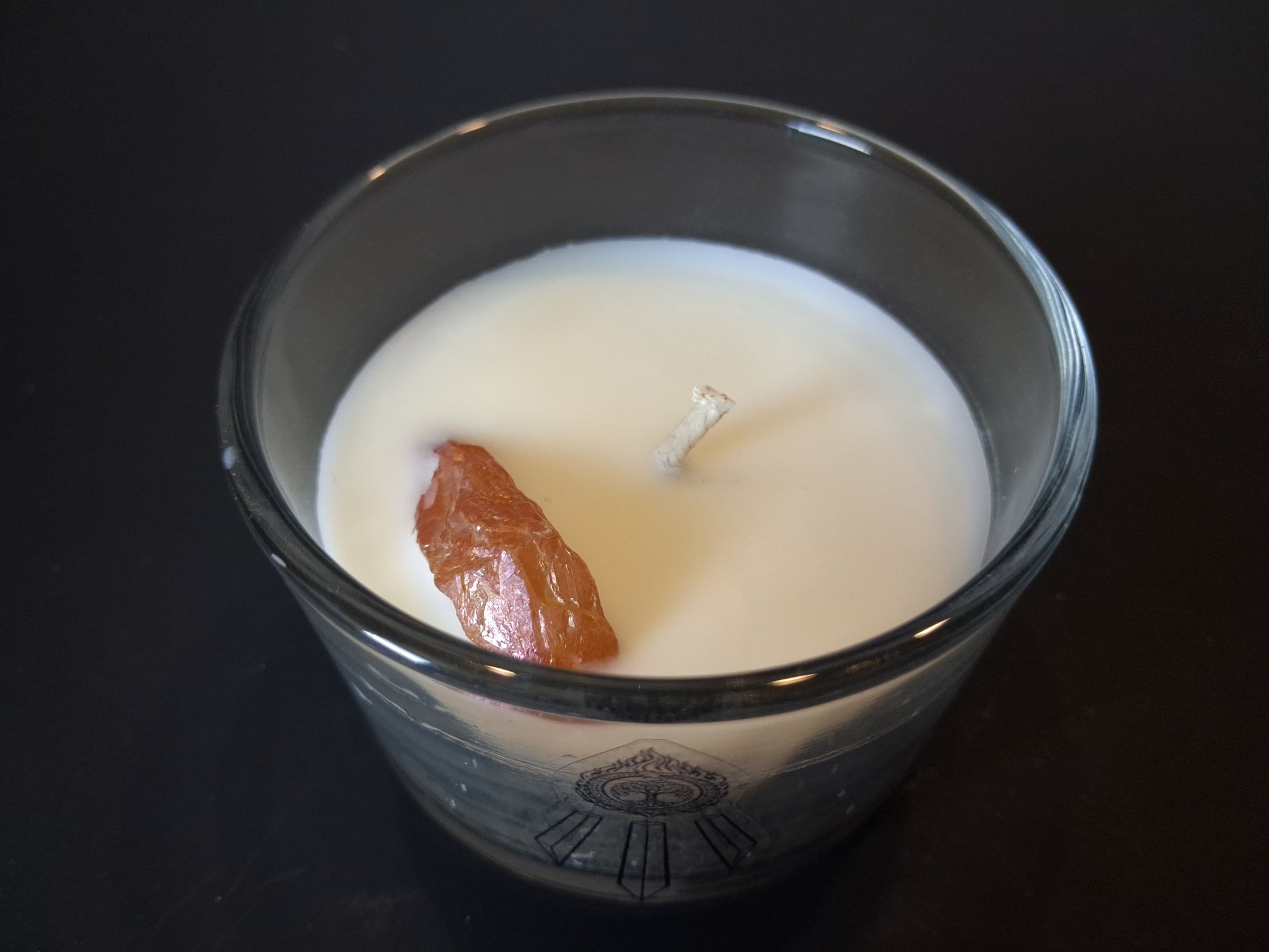 Champagne Aura Intentions candle open from above showing raw champagne aura quartz gemstone and wick set in cream wax, Awen Aboros logo etched on clear glass