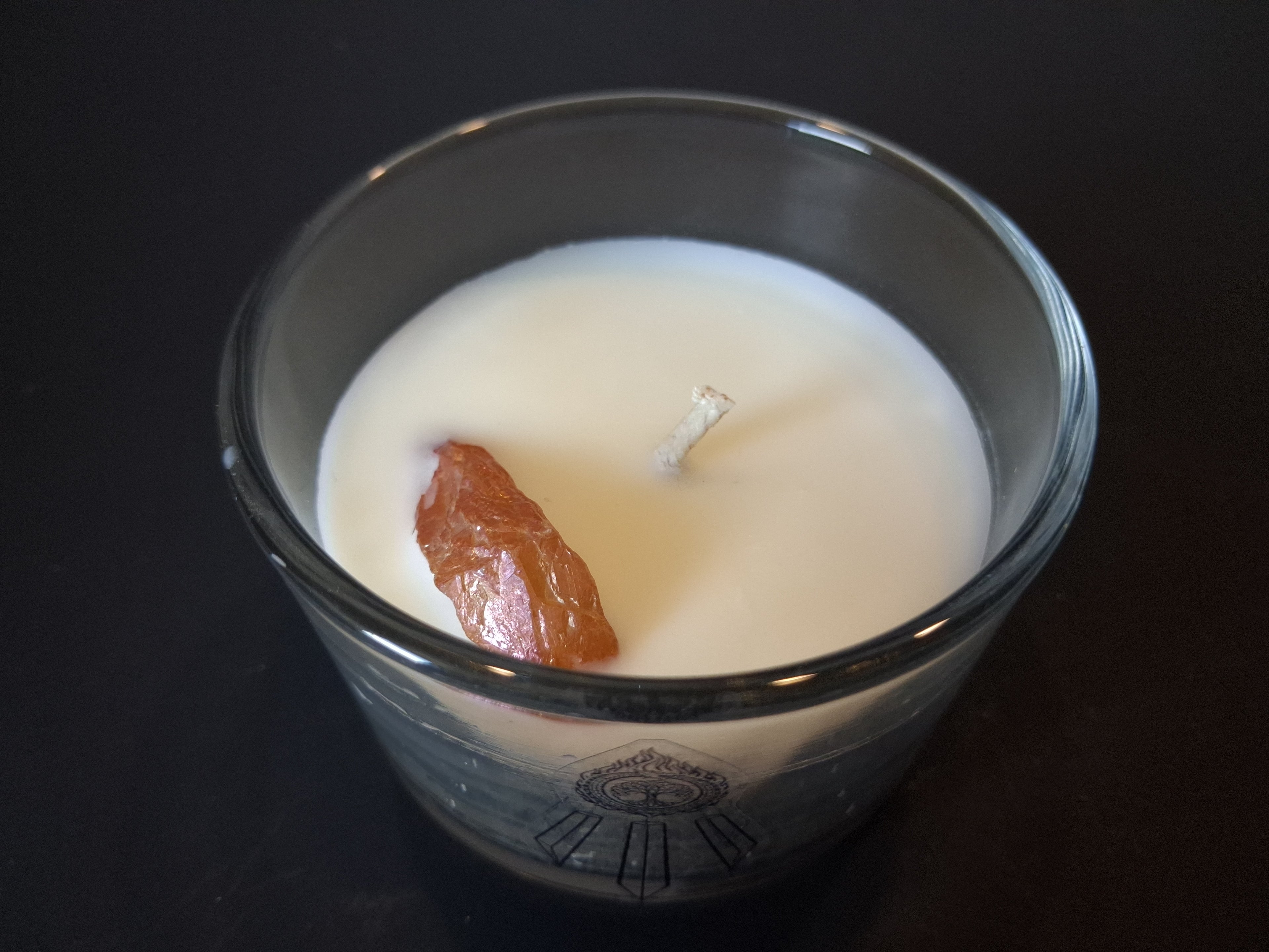 Champagne Aura Intentions candle open from above showing raw champagne aura quartz gemstone and wick set in cream wax, Awen Aboros logo etched on clear glass